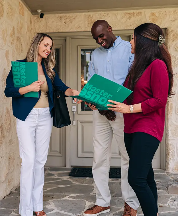 HouseMaster agent standing on porch with two customers holding green folders.