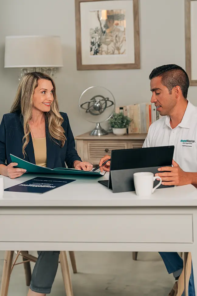 HouseMaster agent sitting at table showing female customer folder and laptop.