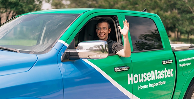 HouseMaster inspector waving inside branded truck.