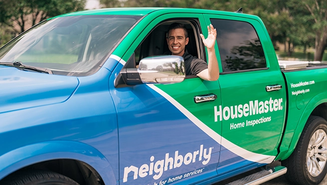 Smiling HouseMaster inspector waving inside of branded truck.