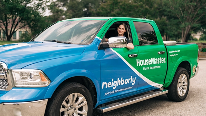 Smiling female HouseMaster inspector inside branded truck.