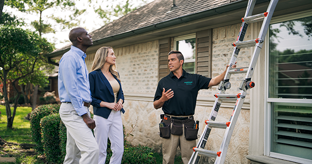 HouseMaster inspector holding ladder talking with couple.