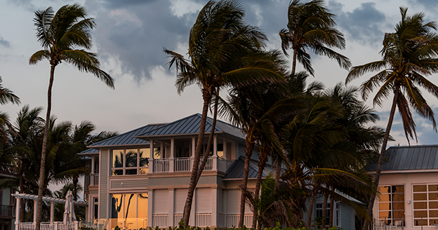 Two story home with palm trees blowing at sunset.