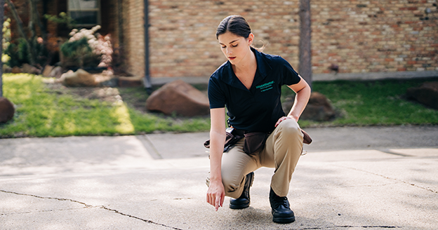 Technician kneeling to inspect driveway cracks