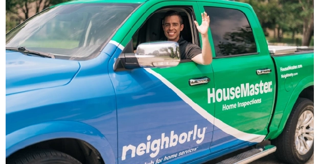 Home inspector waving inside branded HouseMaster-Neighborly truck.