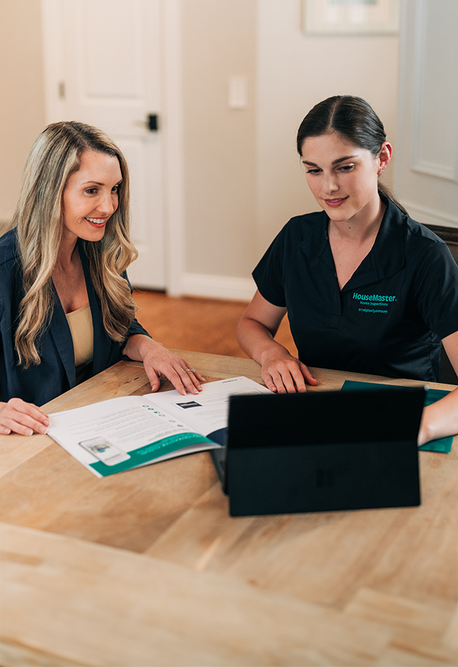 Two women sitting at desk reviewing content on laptop.