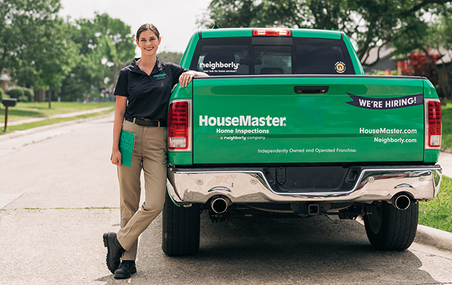 Smiling female HouseMaster inspector leaning against branded truck.