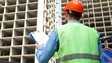Commercial inspector looking up at skyscraper under construction.