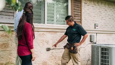 Homebuyers follow a home inspector as he points at a missing exterior outlet cover.