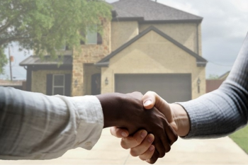 Close-up of people shaking hands in front of a house.