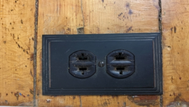 A black electrical outlet on a wood surface.