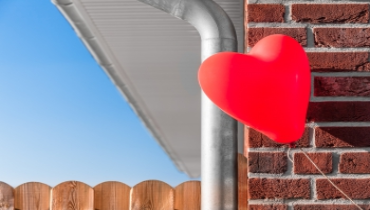 A red heart shaped balloon on a brick wall.