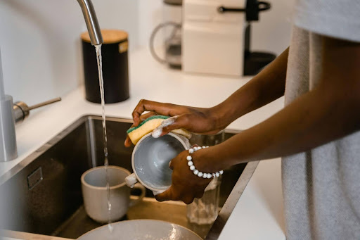 Hands washing dishes at a kitchen sink.