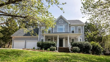 Two story colonial home surrounded by trees and foliage.