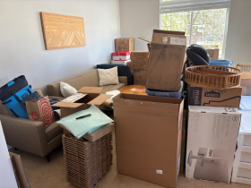 Room filled with moving boxes and packed items stacked around a couch.