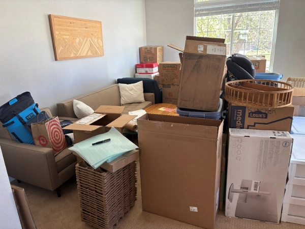 Room filled with moving boxes and packed items stacked around a couch.